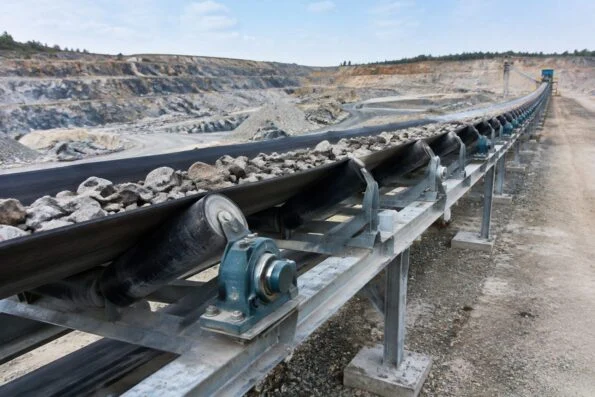 Long belt conveyor running across a quarry site with steel idler frames and pillow block bearing units along the structure