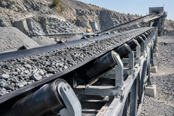 Long belt conveyor carrying crushed aggregate past steel idler frames at a quarry