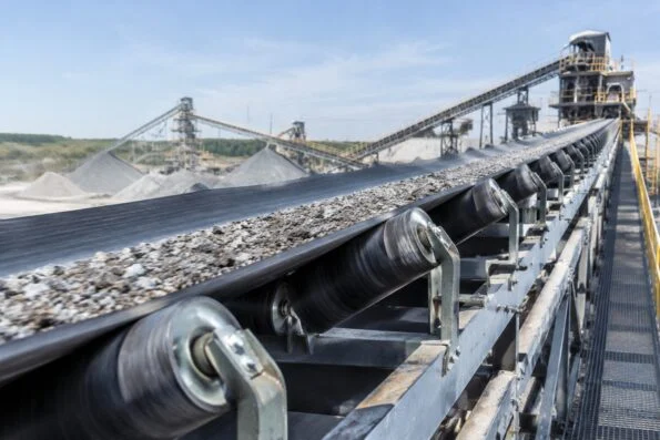 Belt conveyor running across an aggregate plant with idler rollers and steel frame